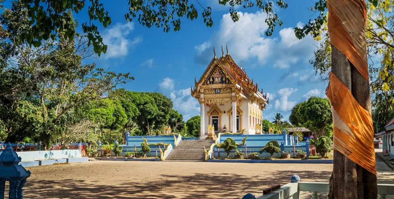 White ordination hall with naga staircase and orange cloth wrapped around a sacred tree
