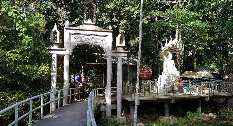 Stone entrance archway reading Wat Namtok Hin Lad, with a white Buddha statue under a naga canopy