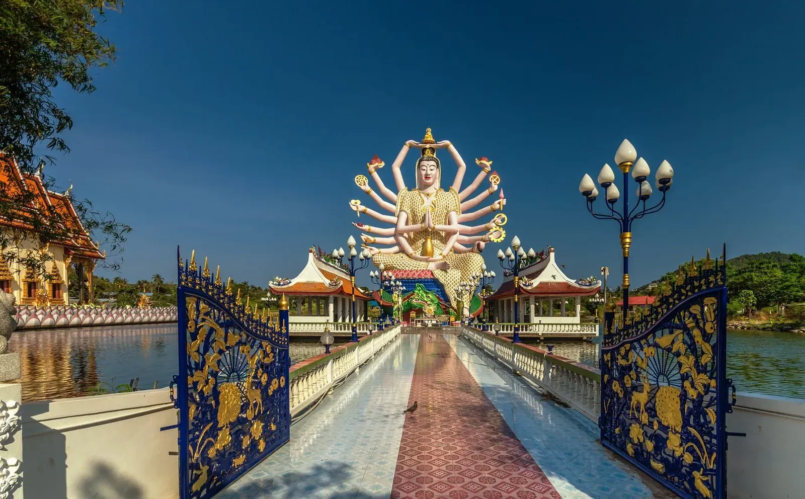 Ornate blue gate framing the 18-armed Guanyin statue and lake at Wat Plai Laem Koh Samui