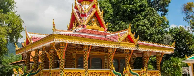 Ornate golden and red gabled pavilion roof of Wat Samret rising above the treeline