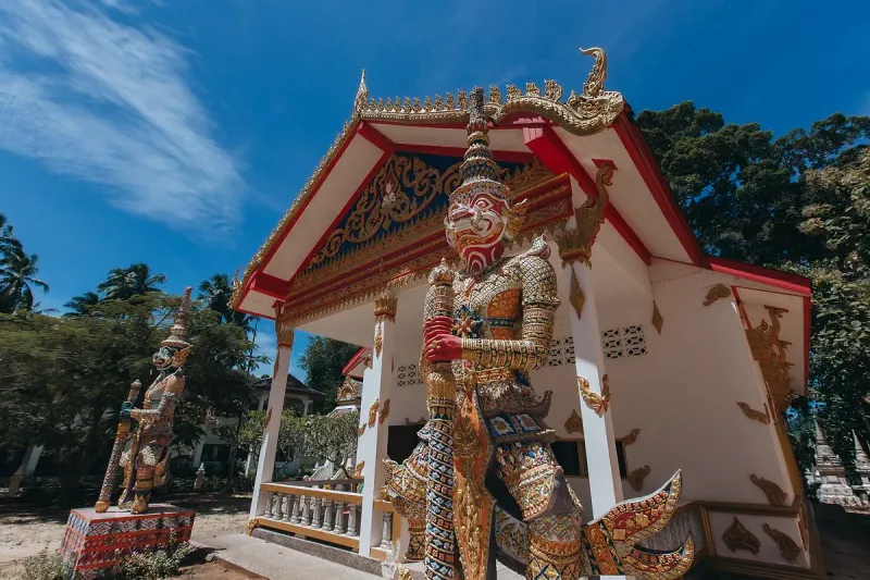 Colorful guardian giant (yaksha) statue standing beside a temple pavilion