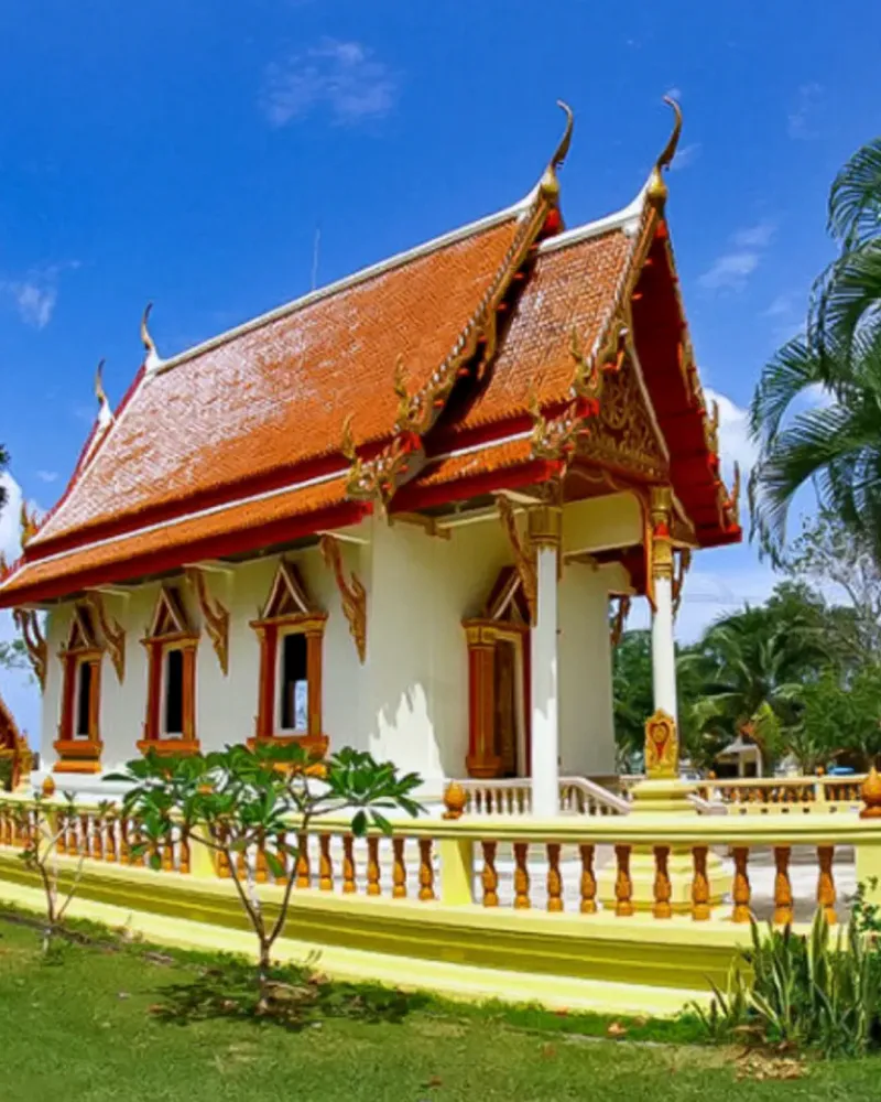 A temple ordination hall with a tiered red-and-gold roof beside a palm tree