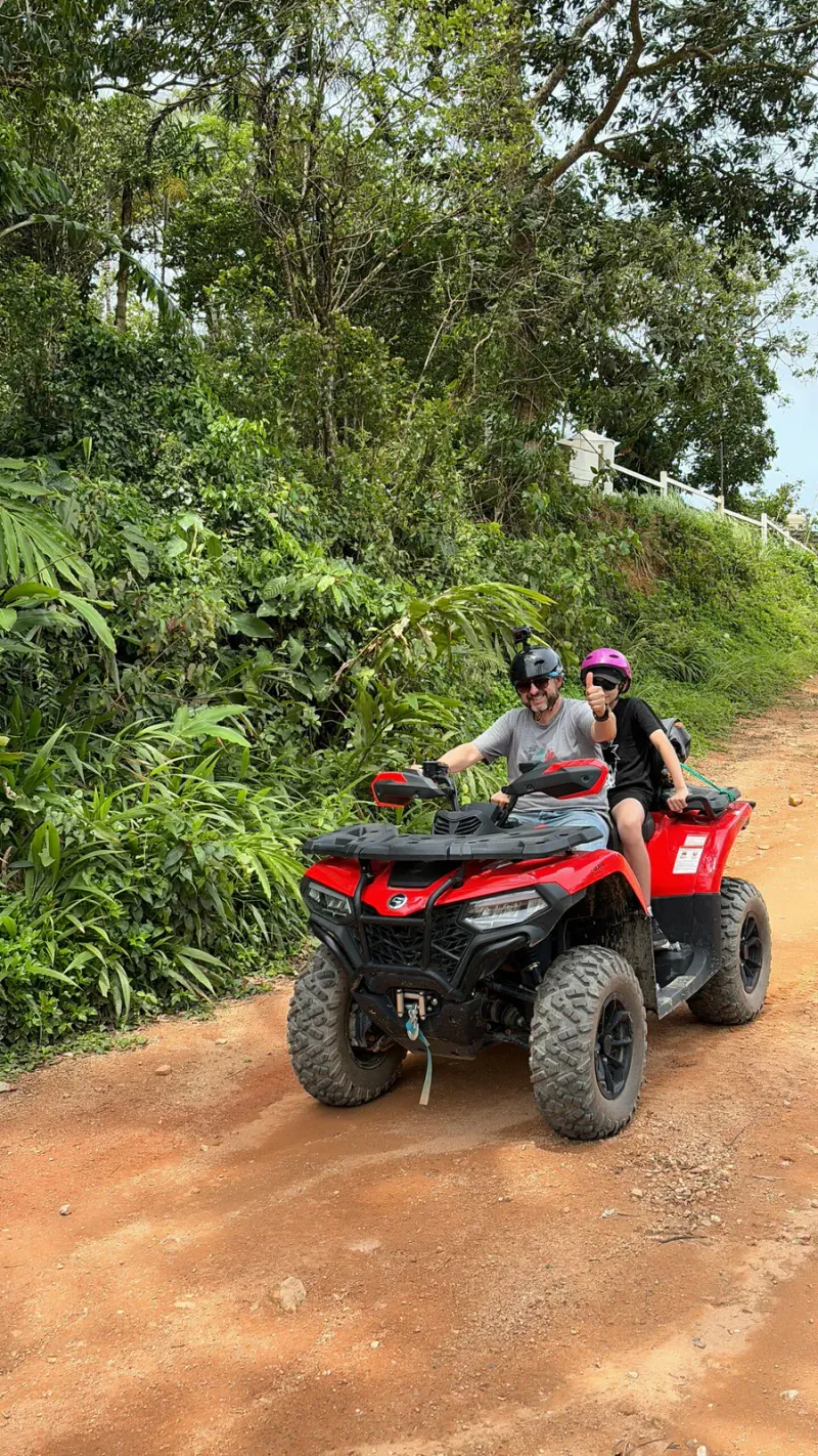 丘の白い柵を背景に、X-Quad Samuiの赤土の道を2人乗りATVで走る参加者
