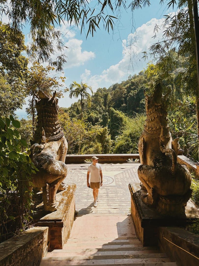 Hiker walking past stone guardian statues on the Secret Buddha Garden Trail Koh Samui jungle path